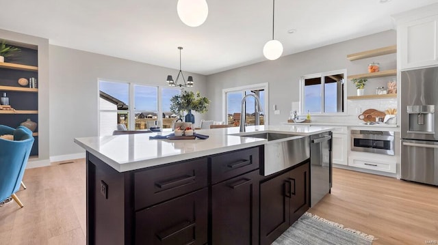 kitchen with appliances with stainless steel finishes, sink, a center island with sink, decorative light fixtures, and white cabinetry