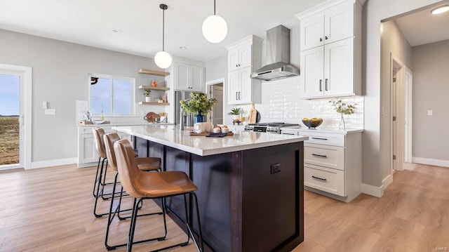 kitchen featuring wall chimney exhaust hood, white cabinetry, light hardwood / wood-style floors, a kitchen island, and hanging light fixtures