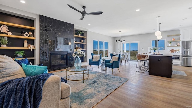 living room with a fireplace, built in features, light hardwood / wood-style floors, and ceiling fan with notable chandelier