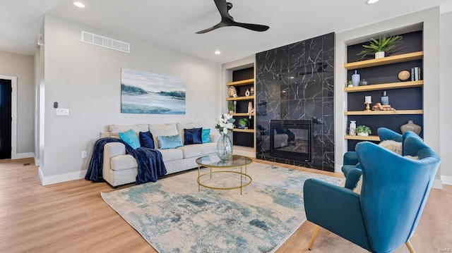 living room with a fireplace, light hardwood / wood-style flooring, built in features, and ceiling fan