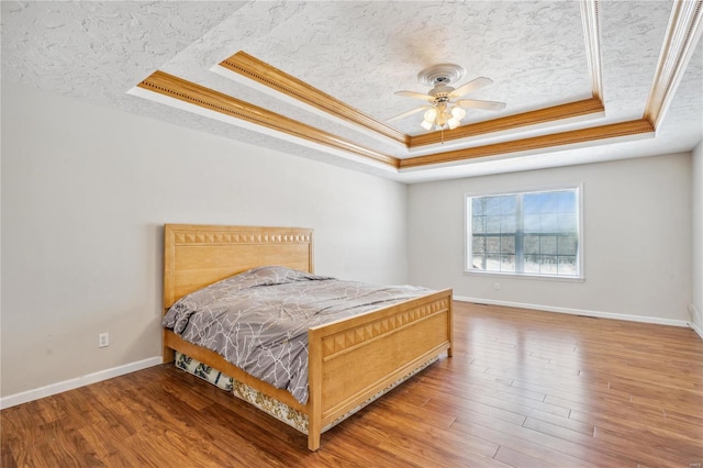 bedroom featuring ceiling fan, a tray ceiling, ornamental molding, and hardwood / wood-style flooring