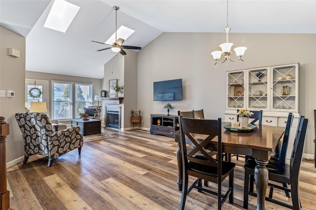 dining area featuring vaulted ceiling with skylight, ceiling fan with notable chandelier, and hardwood / wood-style flooring