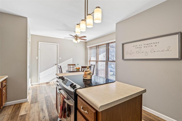 kitchen with pendant lighting, stainless steel electric stove, a kitchen island, dark hardwood / wood-style flooring, and ceiling fan