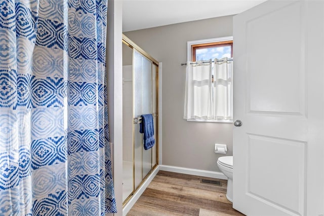 bathroom featuring toilet, an enclosed shower, and wood-type flooring