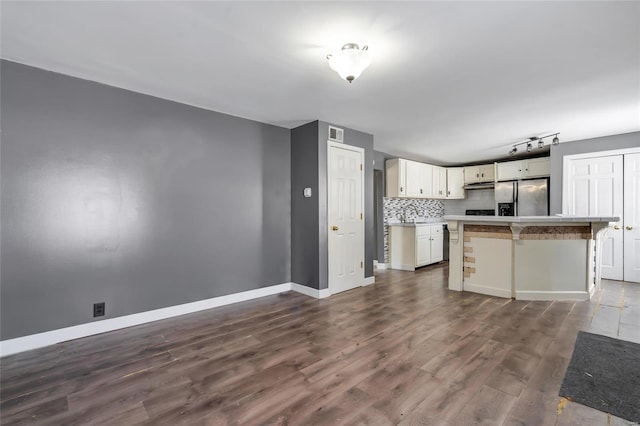 kitchen featuring stainless steel refrigerator with ice dispenser, tasteful backsplash, dark wood-type flooring, a kitchen island, and a breakfast bar