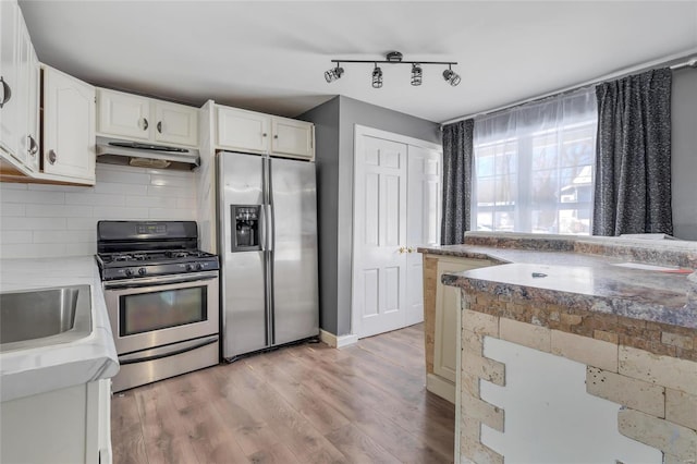 kitchen with backsplash, sink, light hardwood / wood-style flooring, appliances with stainless steel finishes, and white cabinets