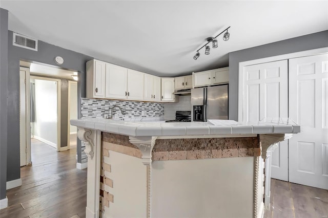 kitchen featuring backsplash, black stove, stainless steel refrigerator with ice dispenser, a breakfast bar area, and tile counters