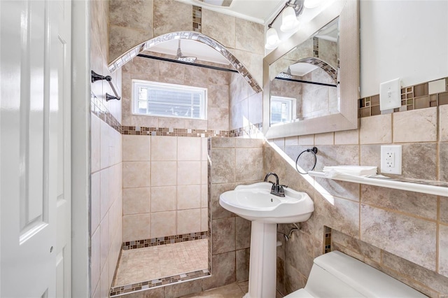 bathroom featuring toilet, decorative backsplash, tiled shower, and sink