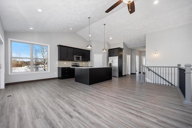 kitchen with wood-type flooring, decorative light fixtures, decorative backsplash, a center island with sink, and appliances with stainless steel finishes