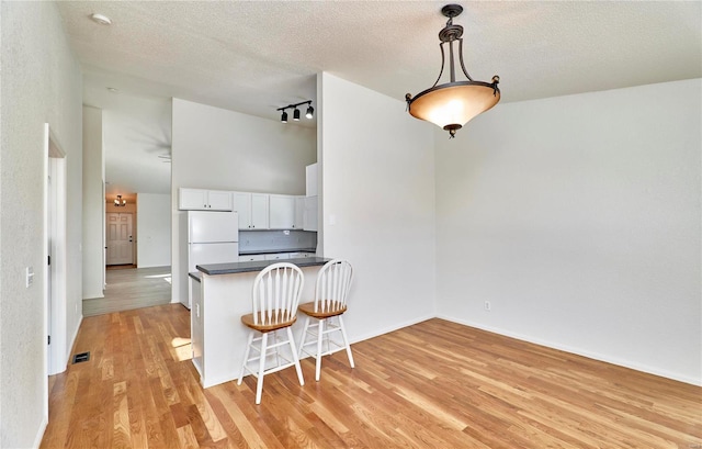 kitchen with pendant lighting, white cabinets, white fridge, kitchen peninsula, and a breakfast bar area