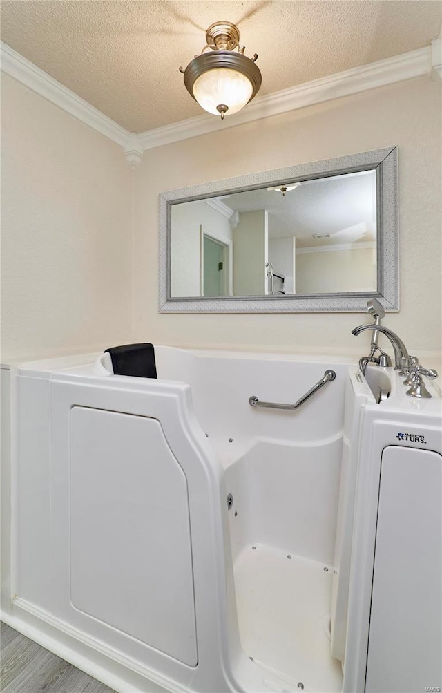 bathroom with a tub, a textured ceiling, ornamental molding, and hardwood / wood-style floors