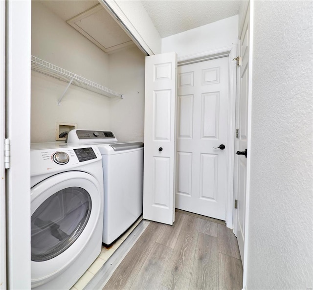 laundry area with a textured ceiling, washer and clothes dryer, and light hardwood / wood-style flooring