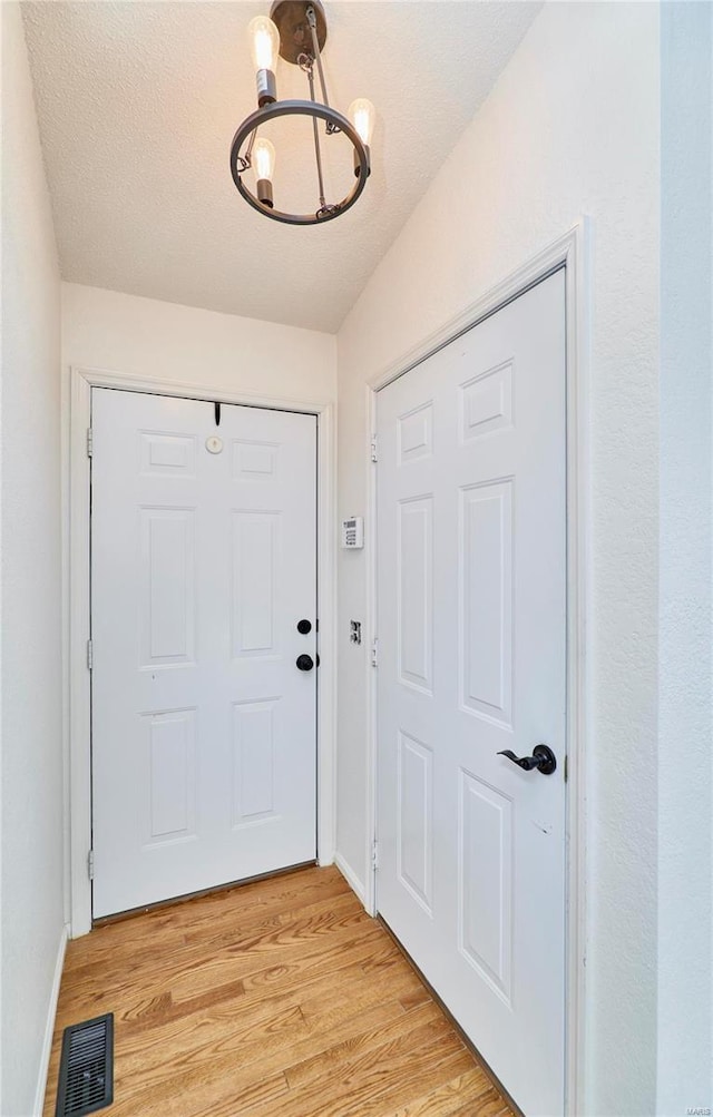 doorway to outside featuring a chandelier, a textured ceiling, light wood-style flooring, visible vents, and baseboards