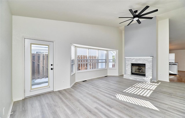 unfurnished living room with baseboards, a ceiling fan, wood finished floors, and a stone fireplace