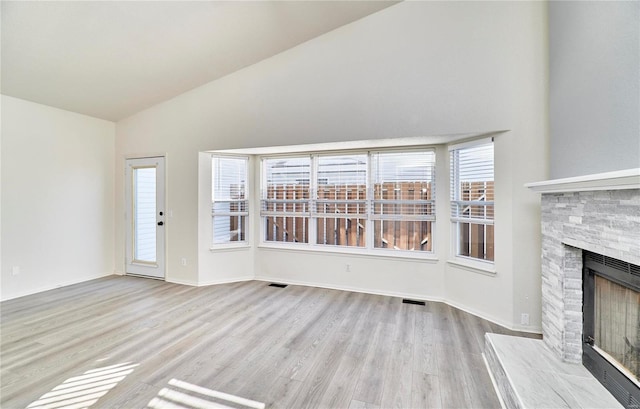 unfurnished living room with high vaulted ceiling, visible vents, wood finished floors, and a stone fireplace