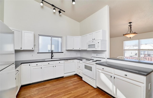 kitchen with dark countertops, vaulted ceiling, a sink, white appliances, and a peninsula