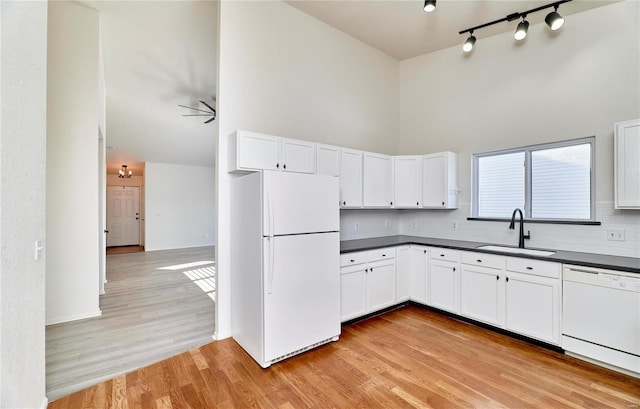 kitchen featuring light wood finished floors, dark countertops, a towering ceiling, a sink, and white appliances