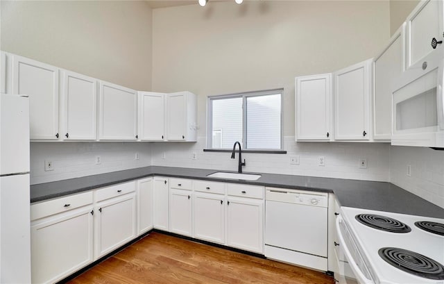 kitchen with dark countertops, white appliances, white cabinetry, and a sink