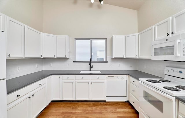 kitchen with light wood finished floors, dark countertops, white cabinetry, a sink, and white appliances