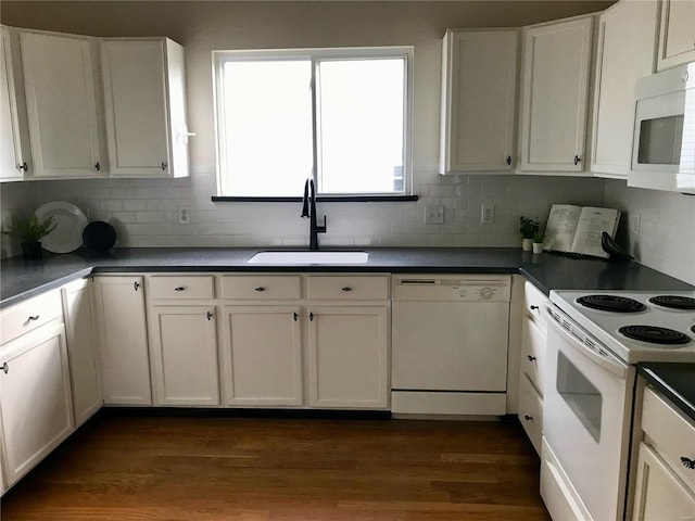 kitchen with dark countertops, dark wood-type flooring, white cabinets, a sink, and white appliances