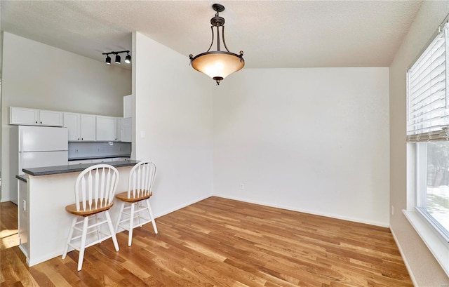 kitchen with white cabinets, freestanding refrigerator, light wood finished floors, dark countertops, and a kitchen bar