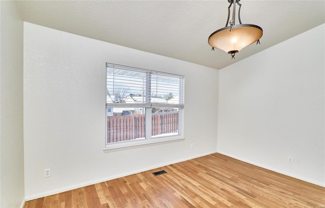 spare room with visible vents, a textured ceiling, baseboards, and wood finished floors