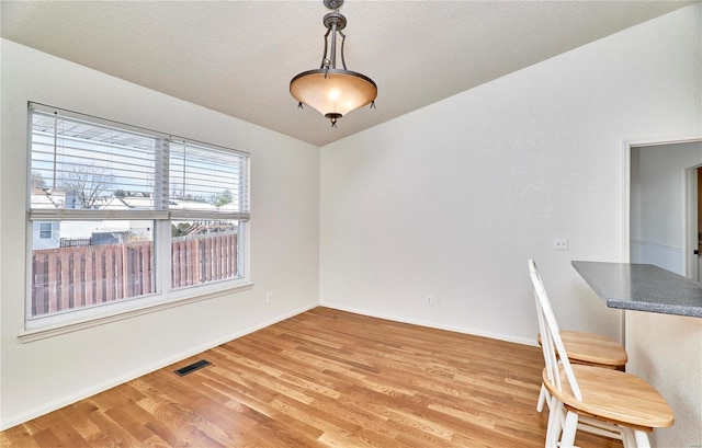 unfurnished dining area with light wood-type flooring, visible vents, a textured ceiling, and baseboards