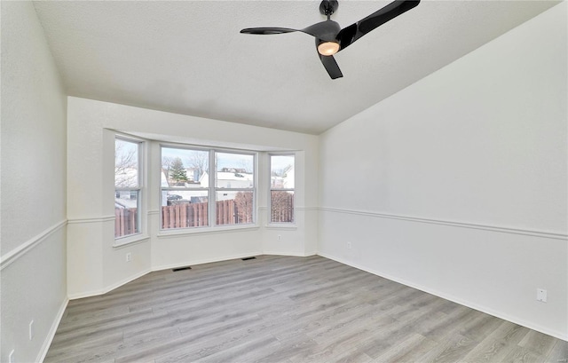 empty room with wood finished floors, visible vents, a ceiling fan, vaulted ceiling, and baseboards