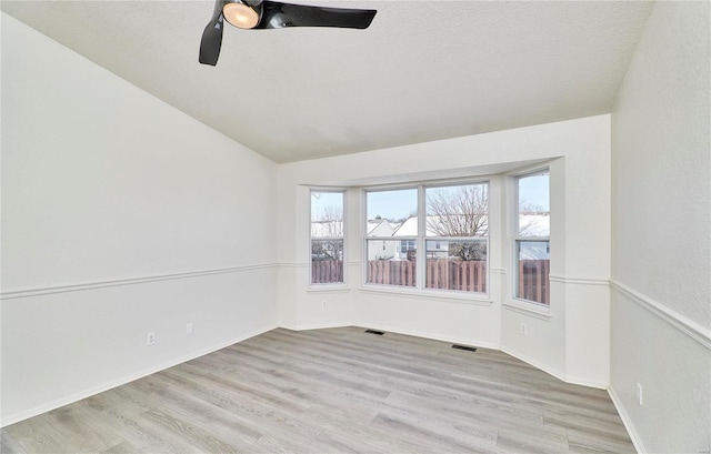 empty room with lofted ceiling, light wood finished floors, plenty of natural light, and a textured ceiling