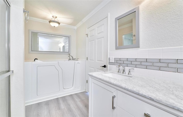 full bath featuring crown molding, backsplash, vanity, wood finished floors, and a bath