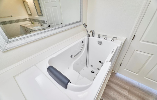 bathroom with a jetted tub, wood finished floors, and vanity