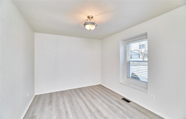 empty room featuring a textured ceiling, baseboards, visible vents, and light wood-style floors