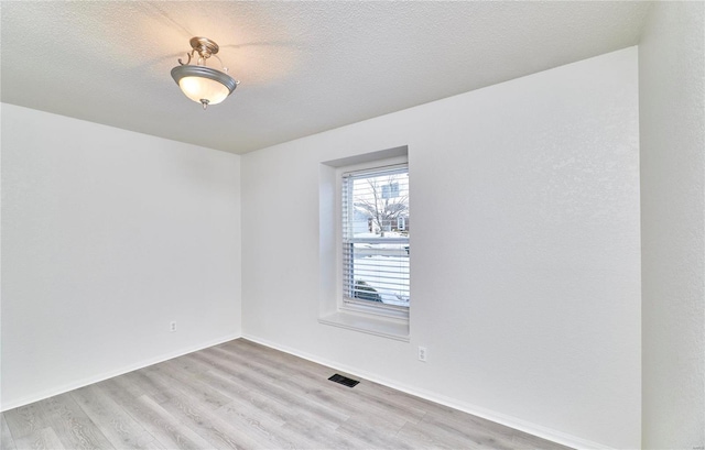 unfurnished room with baseboards, visible vents, light wood-style flooring, and a textured ceiling