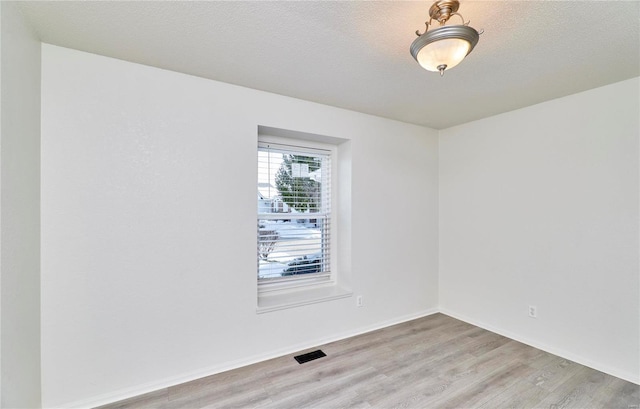 empty room with baseboards, visible vents, light wood-style flooring, and a textured ceiling