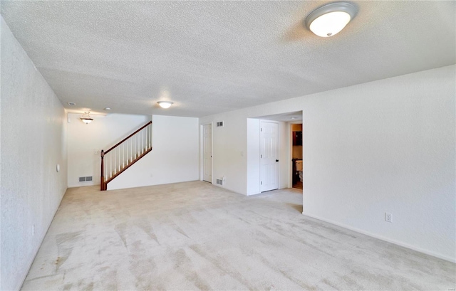 finished below grade area featuring carpet, visible vents, stairway, and a textured ceiling