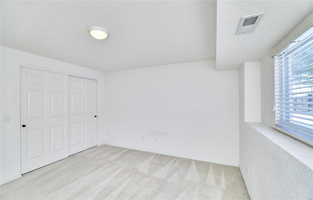 unfurnished bedroom featuring light colored carpet, a closet, visible vents, and a textured ceiling