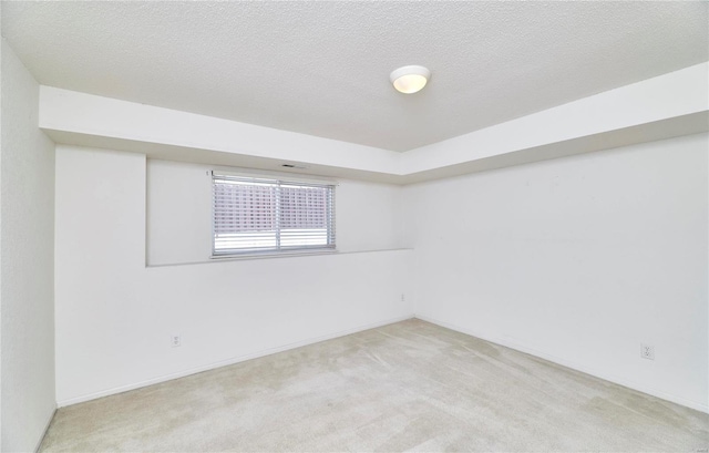 empty room with light carpet, a textured ceiling, and baseboards