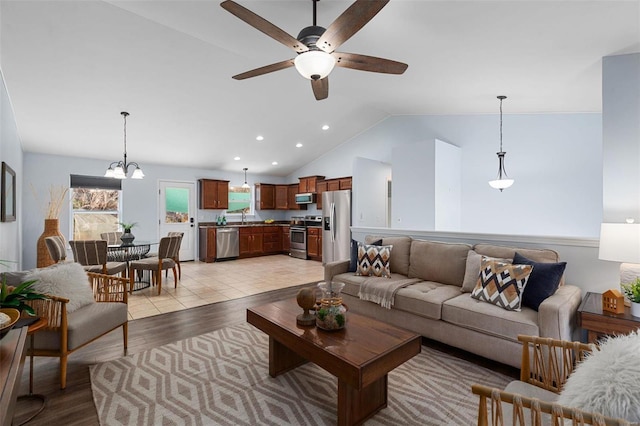 living room featuring ceiling fan with notable chandelier, lofted ceiling, sink, and light hardwood / wood-style floors