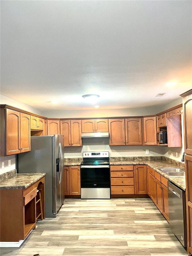 kitchen with stone counters, appliances with stainless steel finishes, light hardwood / wood-style floors, and sink