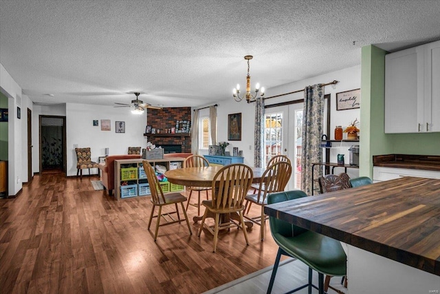 dining space with a fireplace, ceiling fan with notable chandelier, a textured ceiling, and hardwood / wood-style flooring