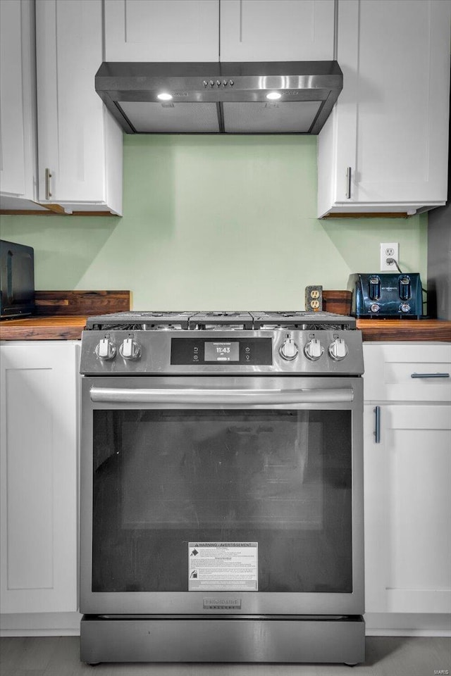 interior details featuring wood counters, white cabinetry, high end stainless steel range, and range hood