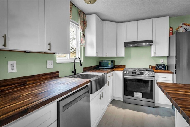 kitchen with butcher block counters, white cabinets, stainless steel appliances, and a textured ceiling