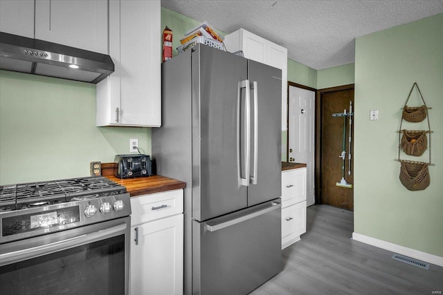 kitchen featuring dark wood-type flooring, white cabinets, a textured ceiling, appliances with stainless steel finishes, and butcher block counters