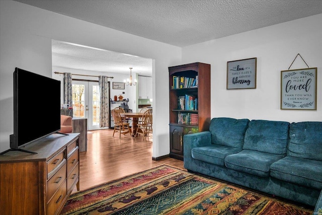 living room featuring a notable chandelier, light wood-type flooring, a textured ceiling, and french doors