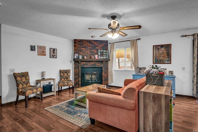 living room featuring ceiling fan, dark hardwood / wood-style flooring, a textured ceiling, and a brick fireplace