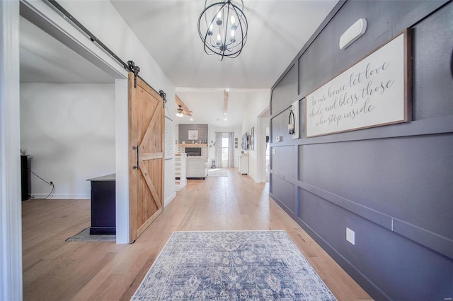 hallway featuring a notable chandelier, light hardwood / wood-style floors, and a barn door