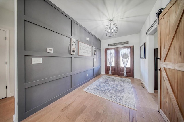 foyer entrance with french doors, a barn door, a chandelier, and light wood-type flooring