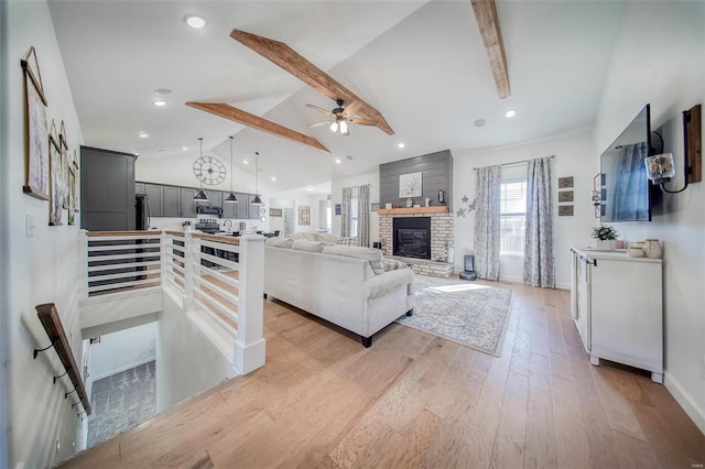 living room featuring ceiling fan, a fireplace, lofted ceiling with beams, and light wood-type flooring