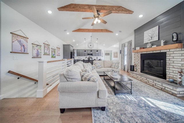 living room featuring wood walls, vaulted ceiling with beams, a brick fireplace, ceiling fan, and light hardwood / wood-style floors