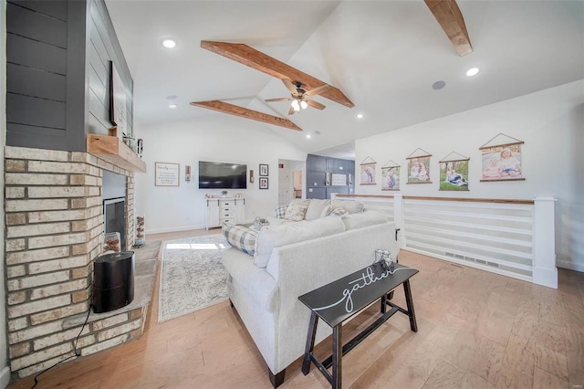 living room featuring ceiling fan, light hardwood / wood-style floors, lofted ceiling with beams, and a brick fireplace